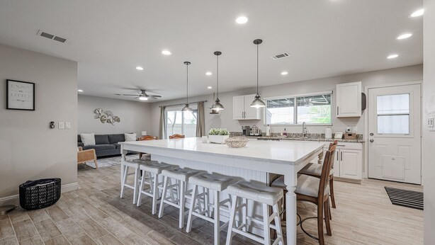 Una cocina moderna con una isla central, taburetes de bar, iluminación colgante y un área de comedor con sofá.