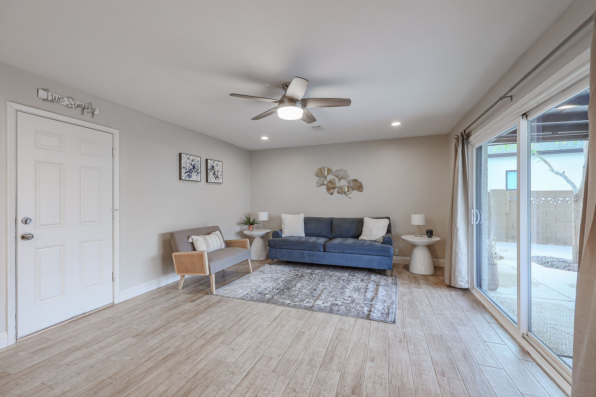 A modern living room with a blue sofa, white walls, and a large window.