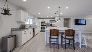 Una cocina moderna con armarios blancos, encimera de granito y una isla central con sillas.