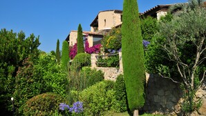 A traditional stone building with a tiled roof, surrounded by lush greenery and various flowering plants.
