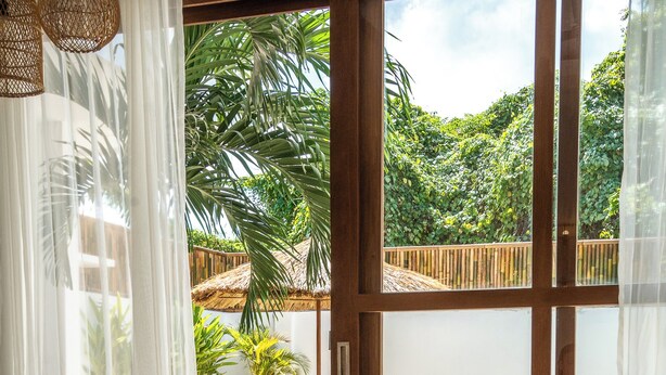 A room with a large sliding glass door leading to an outdoor pool area, wicker furniture, and a woven chair. - Villa Milos (Canggu)