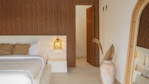 A modern bedroom with a large bed, a bedside lamp, a vase with dried plants, and a wooden panel wall. - Villa Milos (Canggu)