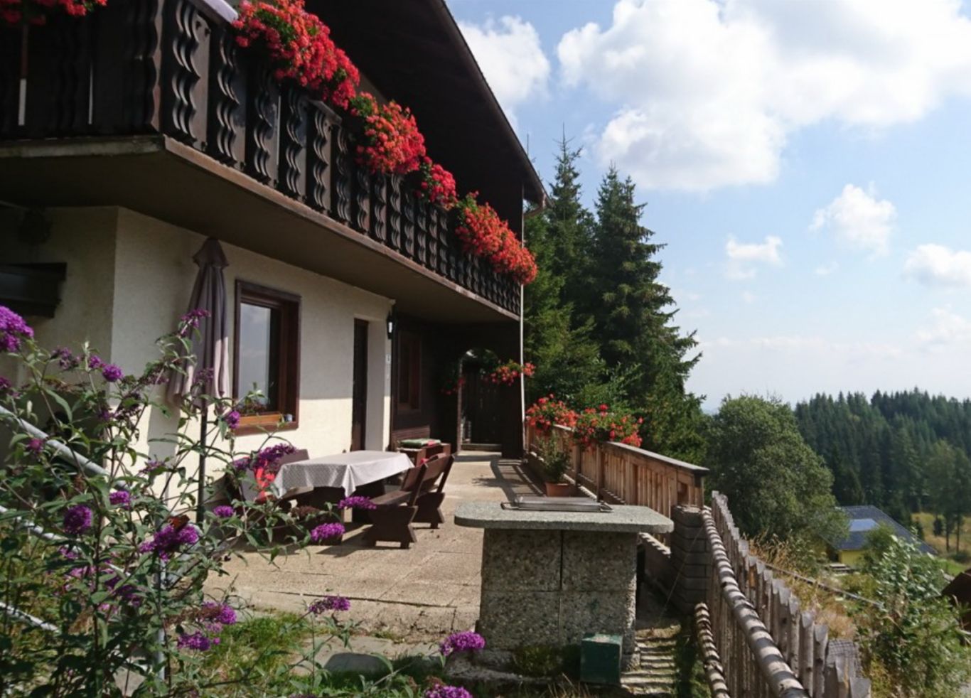 Un edificio a due piani con un balcone decorato da fiori rossi, posti a sedere all'aperto e un muro in pietra.