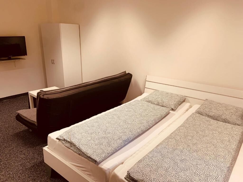 A hotel room with a bed, a chair, a wardrobe, and a TV.