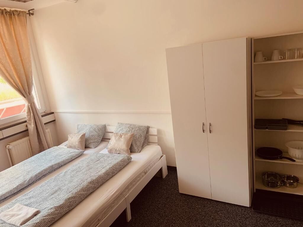 Ein kleines, aufgeräumtes Schlafzimmer mit einem Einzelbett, einem Kleiderschrank und einem Regal mit Geschirr.