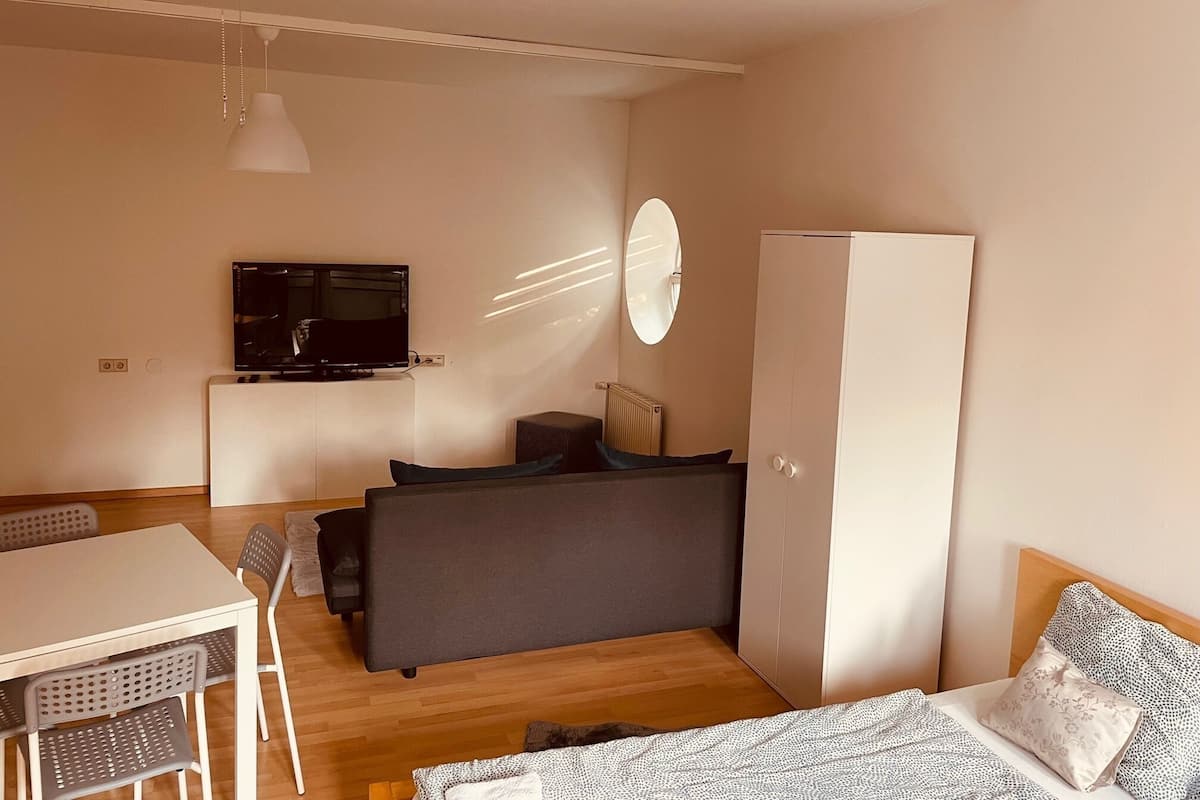 A compact bedroom with a bed, a desk, a chair, a wardrobe, a television, and a mirror.