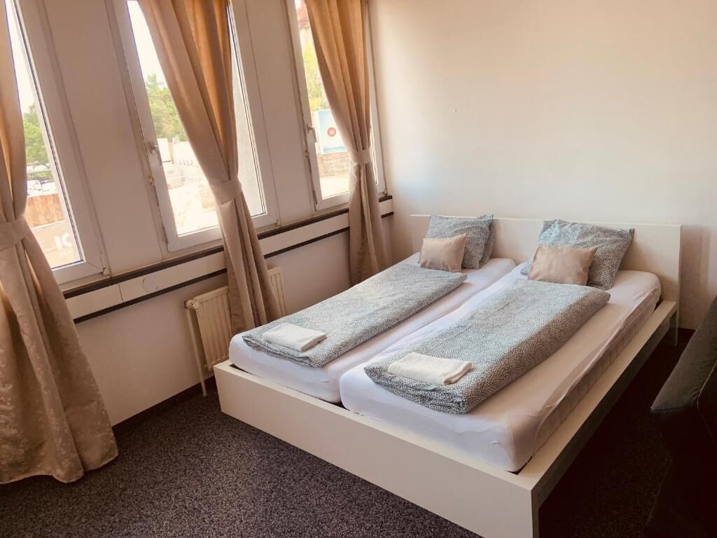 Un lit double avec deux oreillers et une couverture, un radiateur et une fenêtre avec des rideaux.