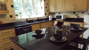 A kitchen with a black countertop, wooden cabinets, a window, and a microwave. - Coventry Park House (Coventry)