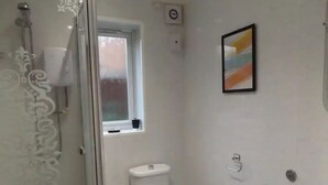 A bathroom with a toilet, a shower, a window, and a sink. - Coventry Park House (Coventry)