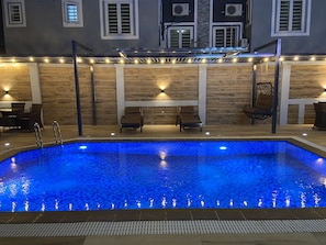 A swimming pool with a blue mosaic tile design, surrounded by lounge chairs and a wooden wall with built-in lighting. - Ivy Hotel Emerald (Lagos)
