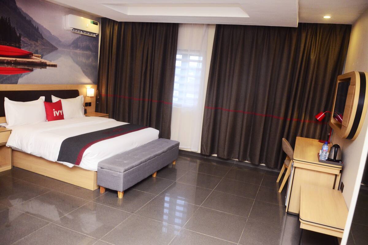 A hotel room with a bed, a small desk, a chair, a mirror, and a window with curtains.
