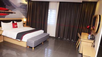 Habitación de hotel con cama, escritorio pequeño, silla, espejo y ventana con cortinas.