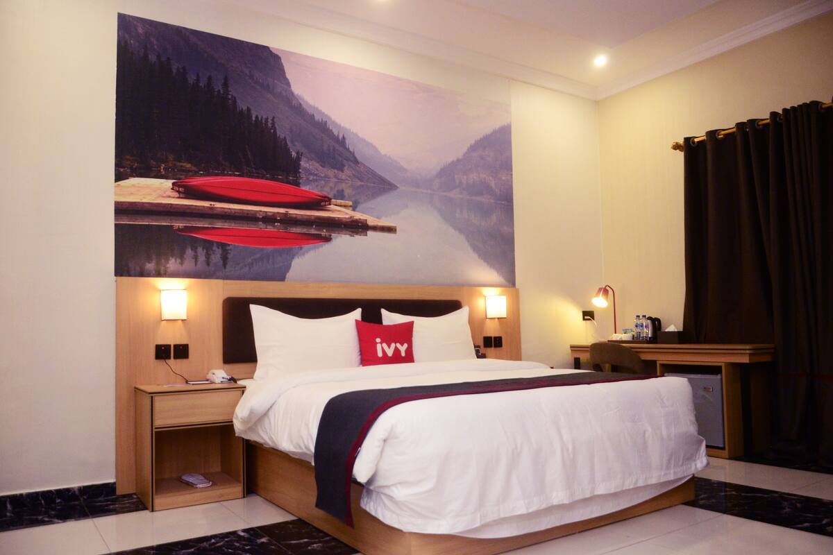 A hotel room with a large bed, a nightstand, a desk, and a wall-mounted TV.