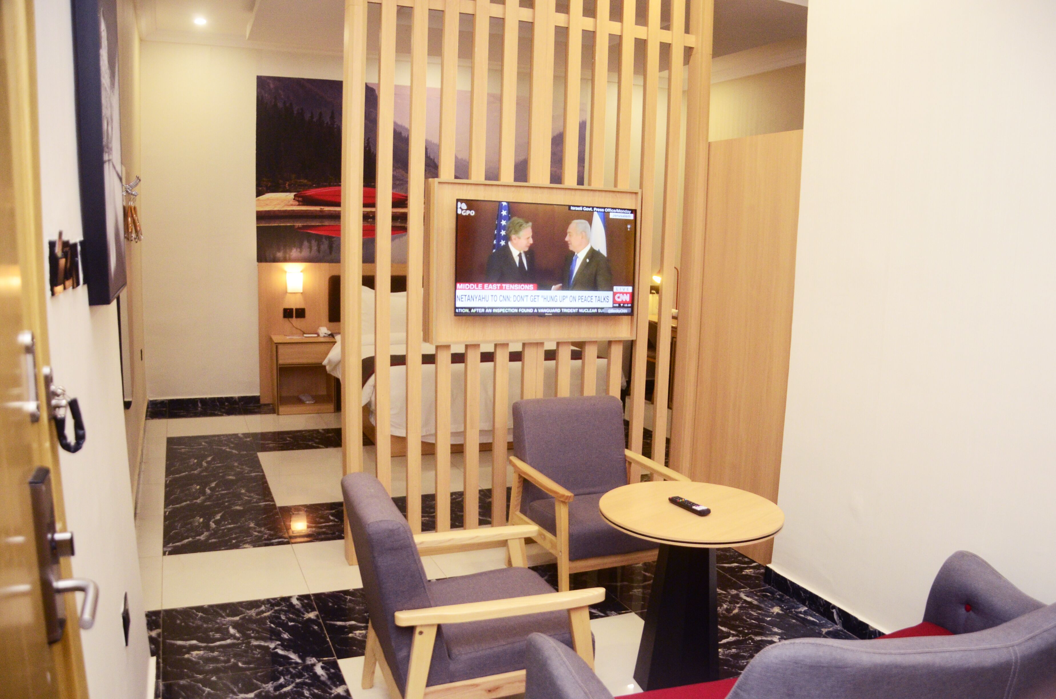 A hotel room with a TV mounted on the wall, a wooden partition, and a seating area with a round table and two chairs.