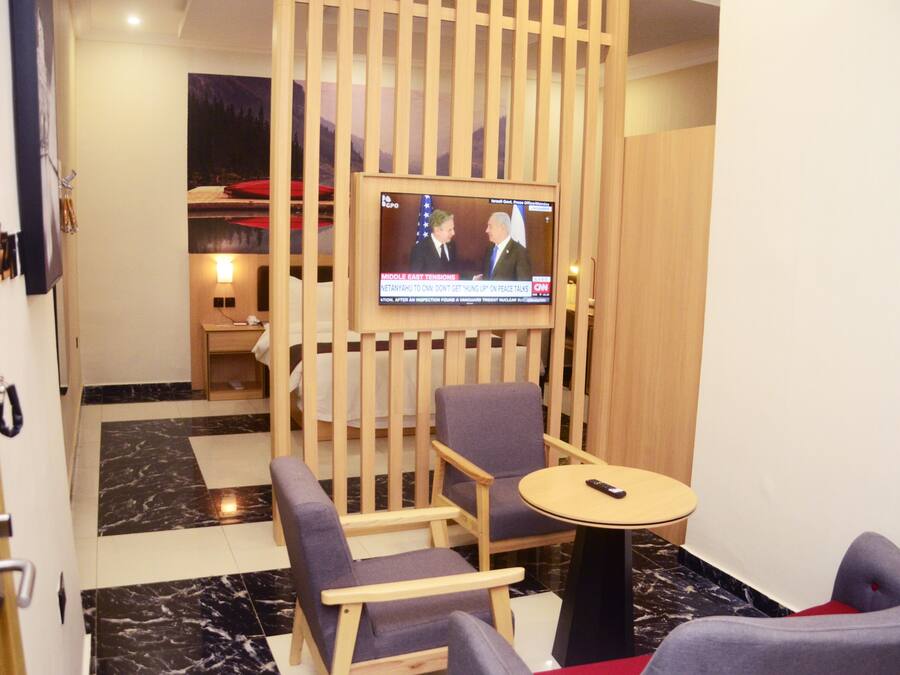 A hotel room with a TV mounted on the wall, a wooden partition, and a seating area with a round table and two chairs.