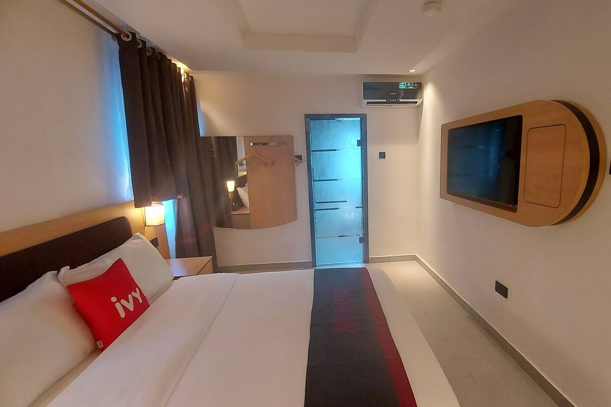 A hotel room with a bed, a TV mounted on the wall, a door, and an air conditioning unit.