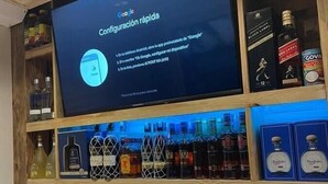 Eine Bar mit einem digitalen Bildschirm, der eine Google-Konfigurationsanleitung zeigt, Regalen mit verschiedenen Spirituosen und einer Holzzahlung.