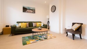 A living room with a green sofa, a round coffee table, a brown armchair, and a painting on the wall. - Immaculate 2-bed House in Dartford (Dartford)