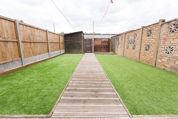 A wooden deck leading to a fenced backyard with artificial grass.