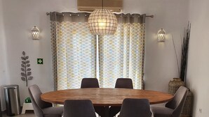 A dining area with a round wooden table, six chairs, a blue rug, patterned curtains, wall-mounted lights, and a decorative plant. - 3 Bedroom (Sleeps 7) Villa in Carvoeiro (Carvoeiro)