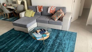 A living room with a grey sectional sofa, a glass coffee table, and a teal rug. - 3 Bedroom (Sleeps 7) Villa in Carvoeiro (Carvoeiro)