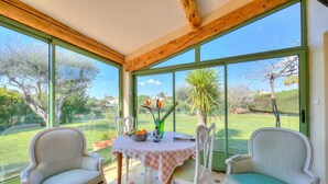 Une véranda avec une table et des chaises, de grandes fenêtres et une vue sur l’extérieur.