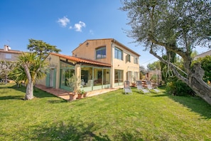 A two-story house with a glass-enclosed patio, a small garden, and a tree.