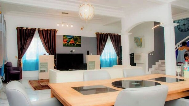 Een moderne woonkamer met een houten eettafel, grijze banken en een flatscreen televisie.