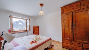 Une chambre à coucher comprenant un lit, une armoire en bois, un bureau, une lampe et une fenêtre donnant sur la montagne.