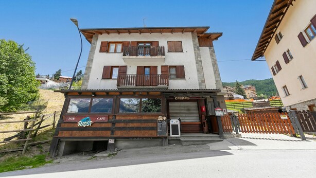 Un bâtiment à deux étages, avec un café-bar au rez-de-chaussée, un balcon à l’étage supérieur et une entrée bien visible.
