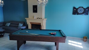Una mesa de billar en una habitación con un sofá, una chimenea y un dardo.