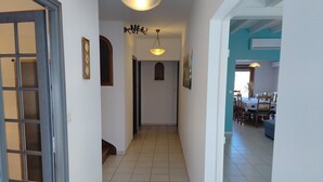 Un pasillo con piso de baldosas, una puerta a la izquierda y un comedor con sillas y una mesa a la derecha.