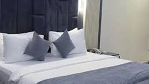 En pænt redt seng med hvide sengetæppe og to puder, et sengebord med en lampe, og et vindue med gardiner.