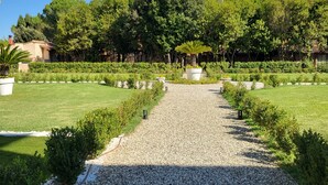 A gravel pathway leading through a well-maintained garden with neatly trimmed hedges and a variety of trees.