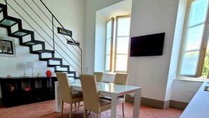 A spacious living area with a modern staircase, a dining table with chairs, and a flat-screen TV mounted on the wall.