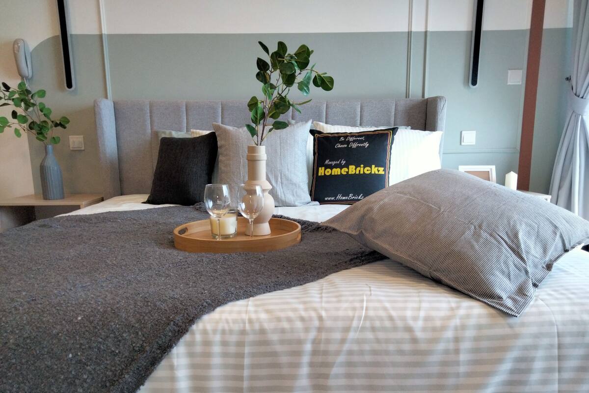 A neatly arranged bedroom with a bed, pillows, a bedside table, a vase with a plant, and a tray with glasses and a candle.