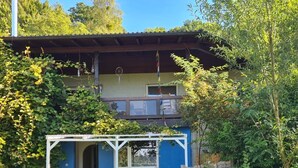 Een huis met een blauwe gevel, een witte veranda en een tuin vol planten en bloemen.
