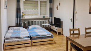 Een compacte, net kamer met twee houten bedden, een tafeltje, een televisie en een radiator.