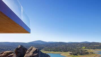 A modern building with a large glass facade overlooking a scenic landscape with mountains and a lake.