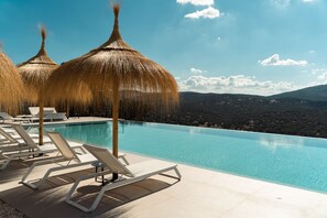 Un espace piscine doté de chaises longues et de parasols en chaume, offrant une vue sur un paysage montagneux.