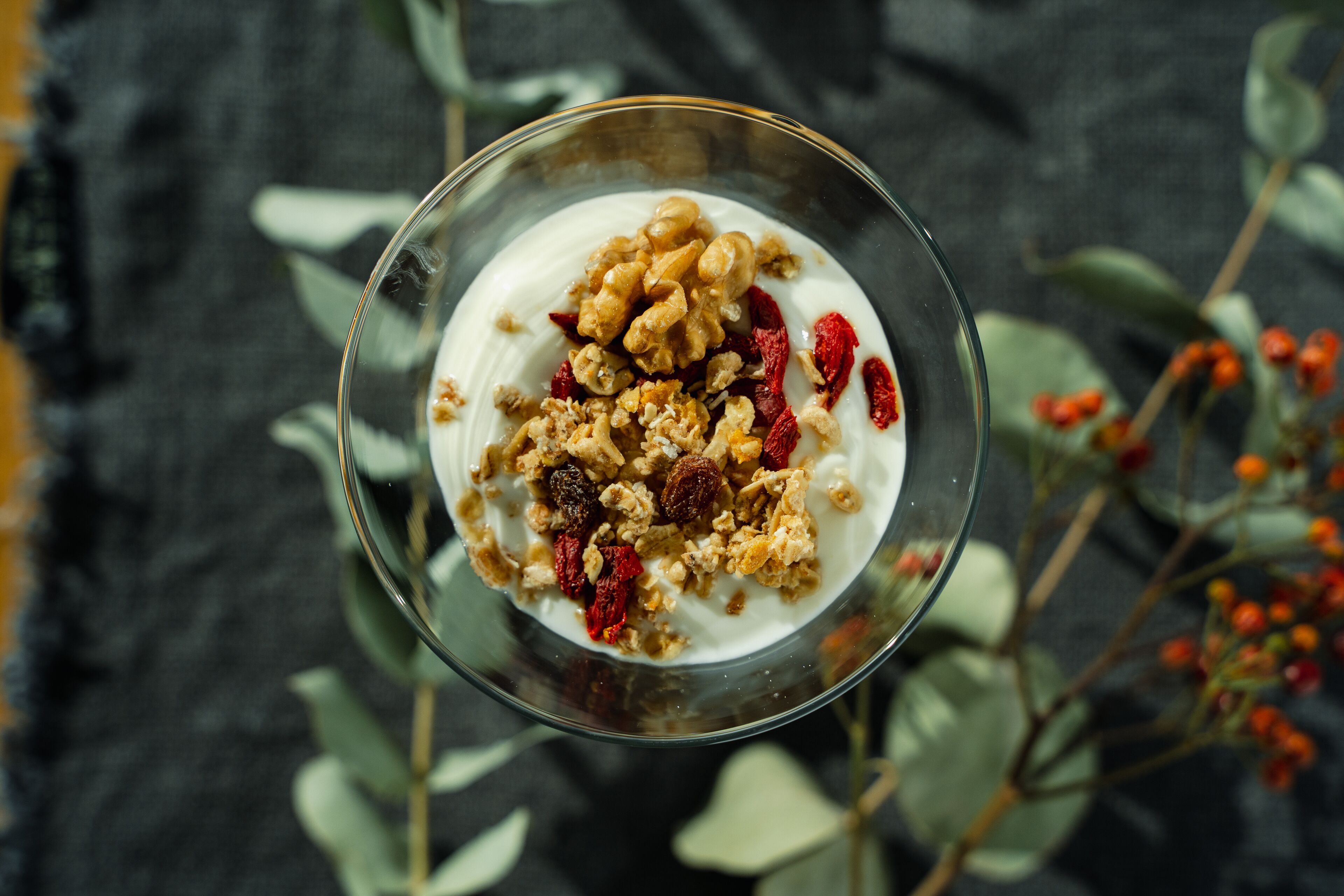 A glass bowl of yogurt with granola and dried fruit.