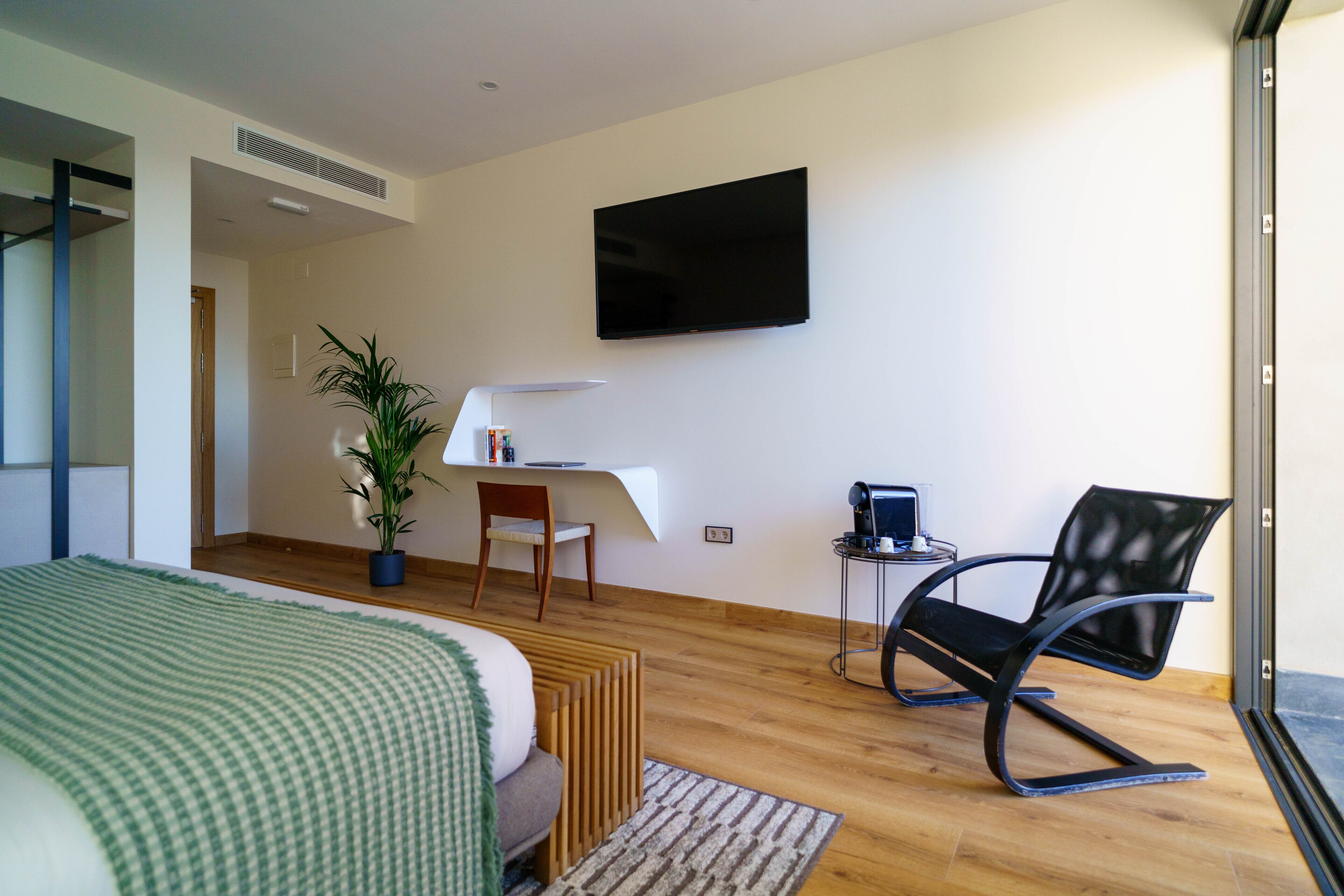 Una habitación de hotel moderna con una cama, un escritorio, una silla, una planta en maceta y un televisor en la pared.