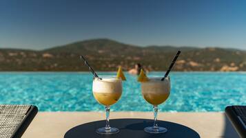 Zwei Cocktails auf einem Tisch neben einem Pool mit Blick auf die Berge.