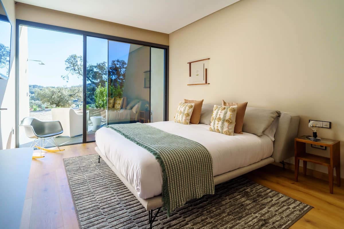 Un dormitorio moderno con una cama grande, un escritorio y vistas a un área exterior por medio de una puerta corrediza de vidrio.