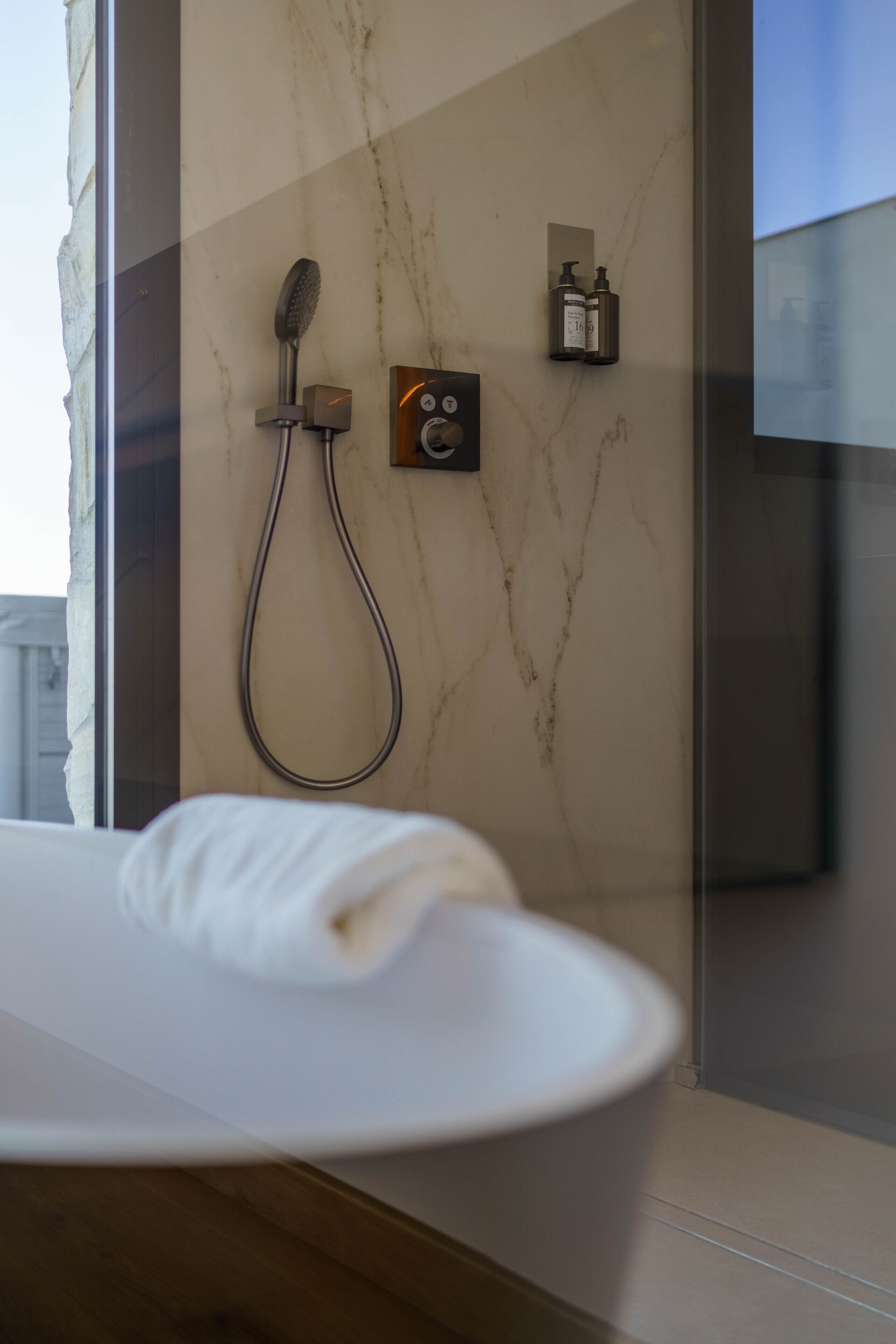 Un baño moderno con pared de mármol, ducha y panel de control.