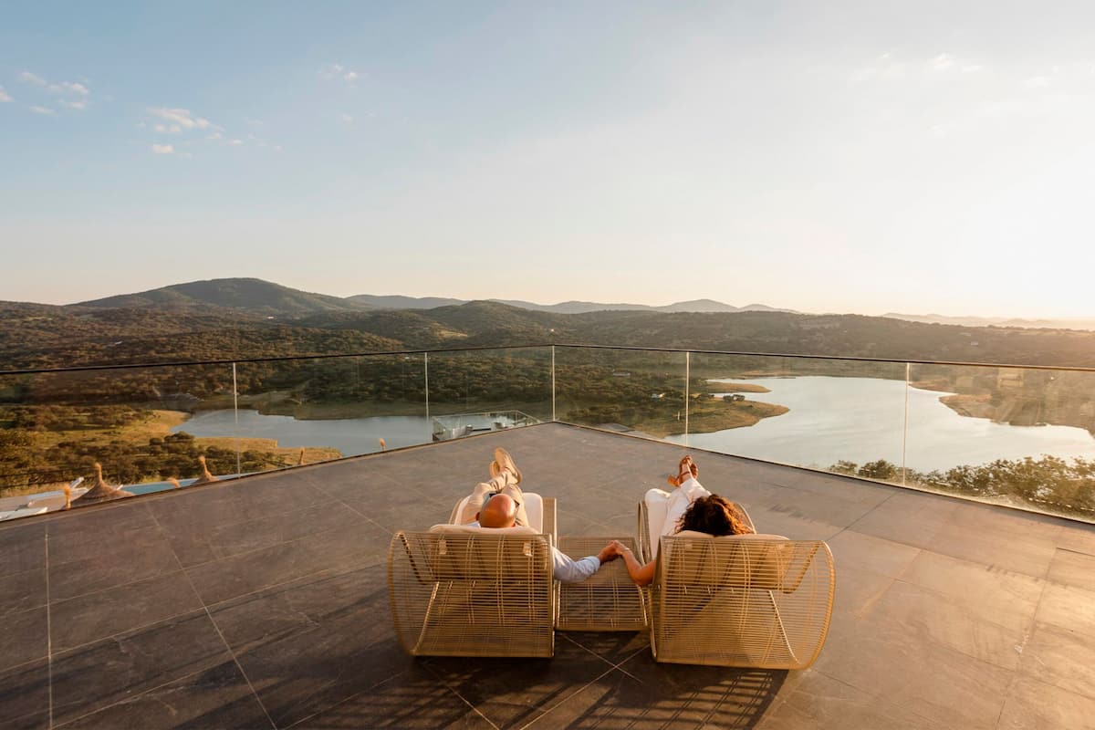Una terraza con sillas de mimbre con vistas a un lago y colinas.