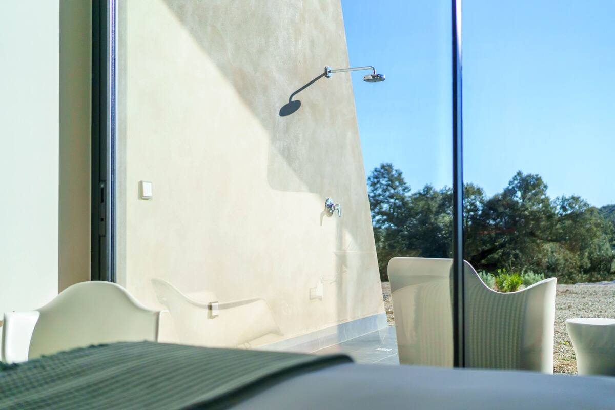 Un baño moderno con ducha, un ventanal grande y vistas a árboles.
