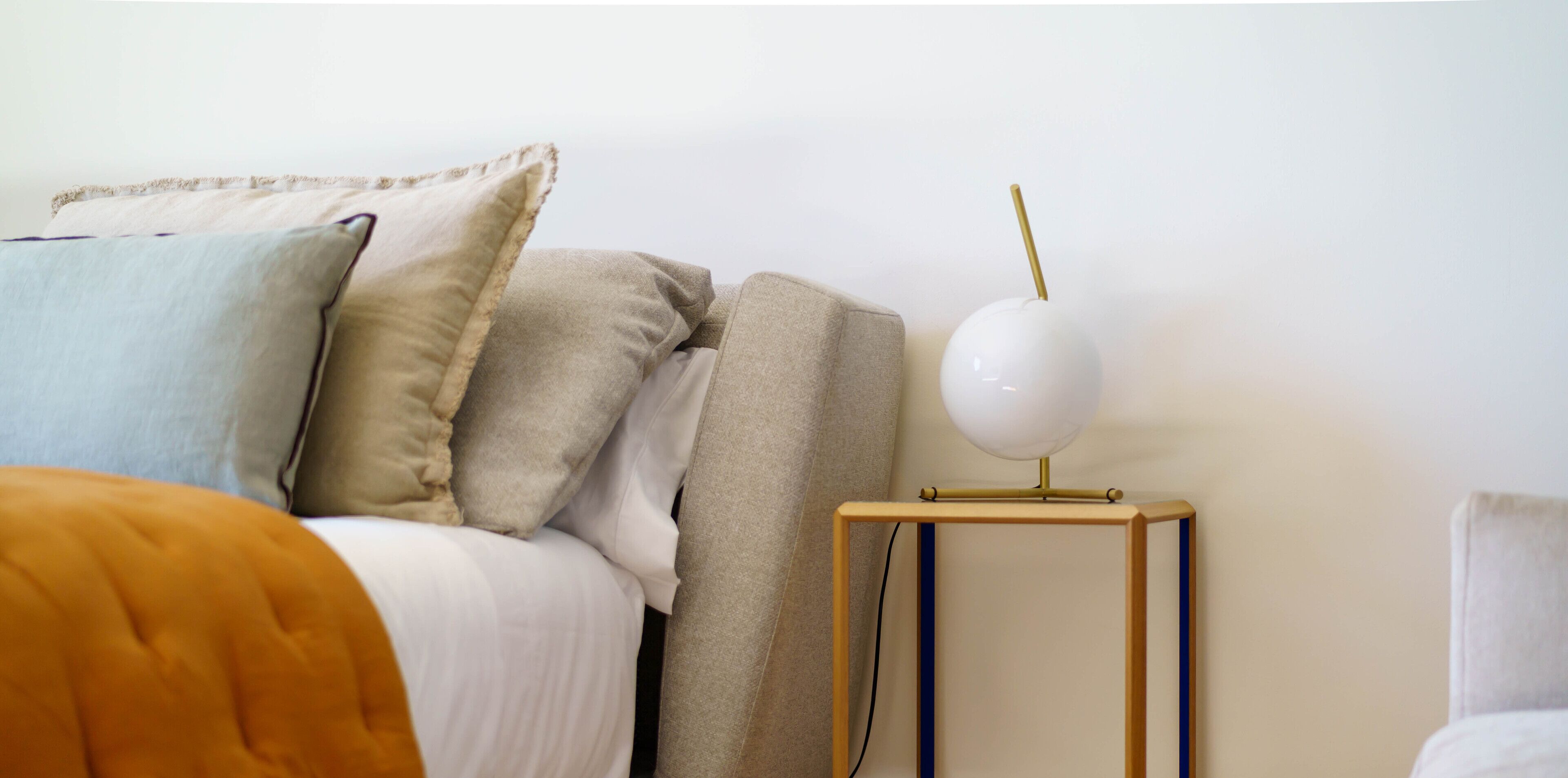 A neatly arranged bedroom with a bed, pillows, a bedside table with a lamp, and a chair.