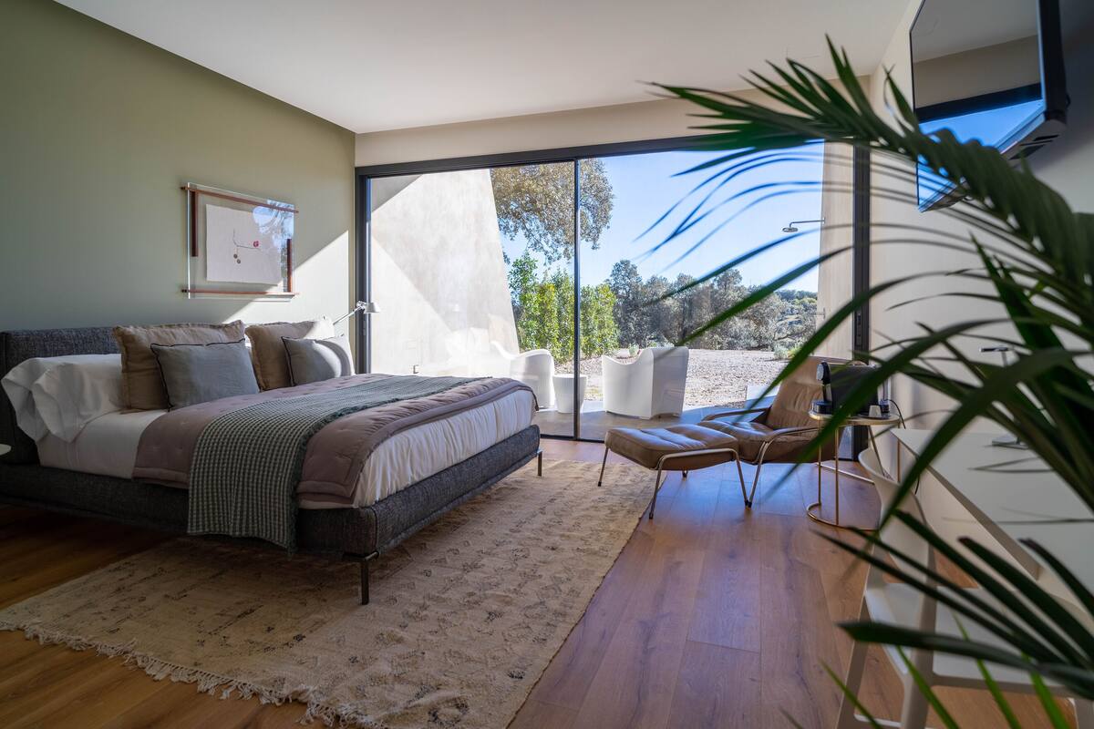 Un dormitorio con cama, una silla y un ventanal grande.