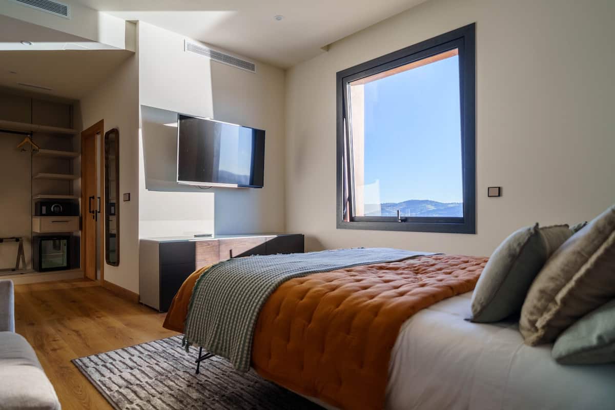 Un dormitorio con cama, televisión, escritorio y un ventanal grande.